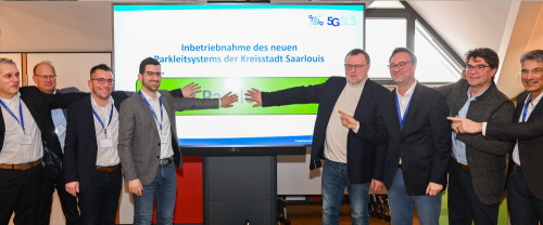 Acht Menschen (Dr. Ralf Levacher, Helmut Bier, Oberbürgermeister Marc Speicher, Bürgermeister Carsten Quirin, Prof. Dr. Horst Wieker, Bundestagsabgeordneter Oliver Luksic, Beigeordneter Gerald Purucker und Prof. Dr. Antonio Krüger) drücken gemeinsam den digitalen Startknopf auf einem Flat-Screen für die Inbetriebnahme des neuen Parkleitsystems der Kreisstadt Saarlouis.