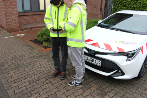 Zwei Personen nehmen Einstellungen an der Drohne vor einem Auto vor.